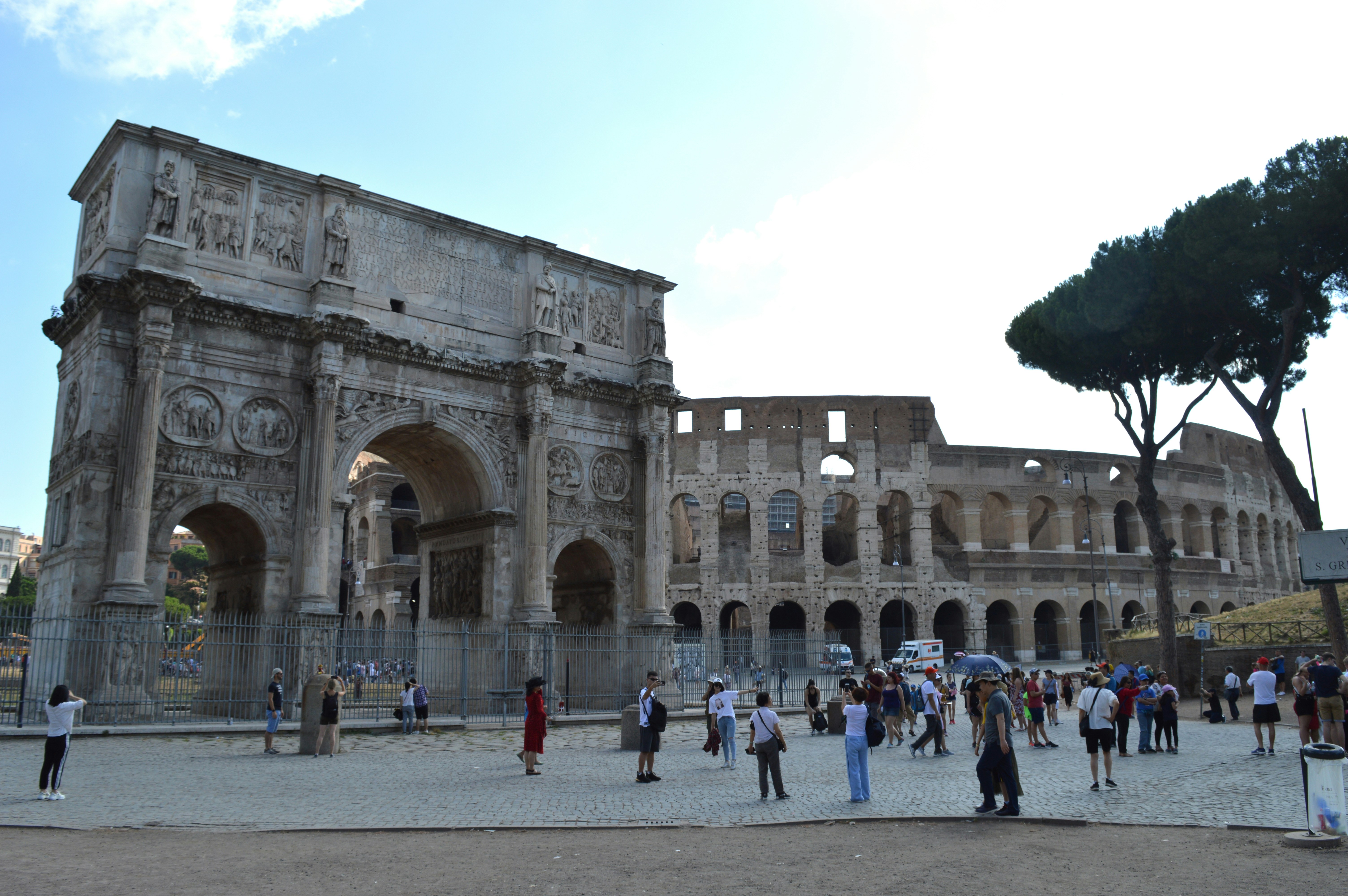 A group of people standing in front of a building, The Colosseum, also known as the Flavian Amphitheatre, is an iconic symbol of ancient Rome, constructed between 70-80 AD under Emperor Vespasian and completed by his son, Titus. This elliptical amphitheater, capable of seating 50,000 to 80,000 spectators, hosted gladiatorial contests, public spectacles, and mock sea battles, showcasing the grandeur of Roman entertainment. Despite suffering damage from earthquakes and stone robbers, the Colosseum remains a UNESCO World Heritage site and one of the most visited tourist attractions in the world.