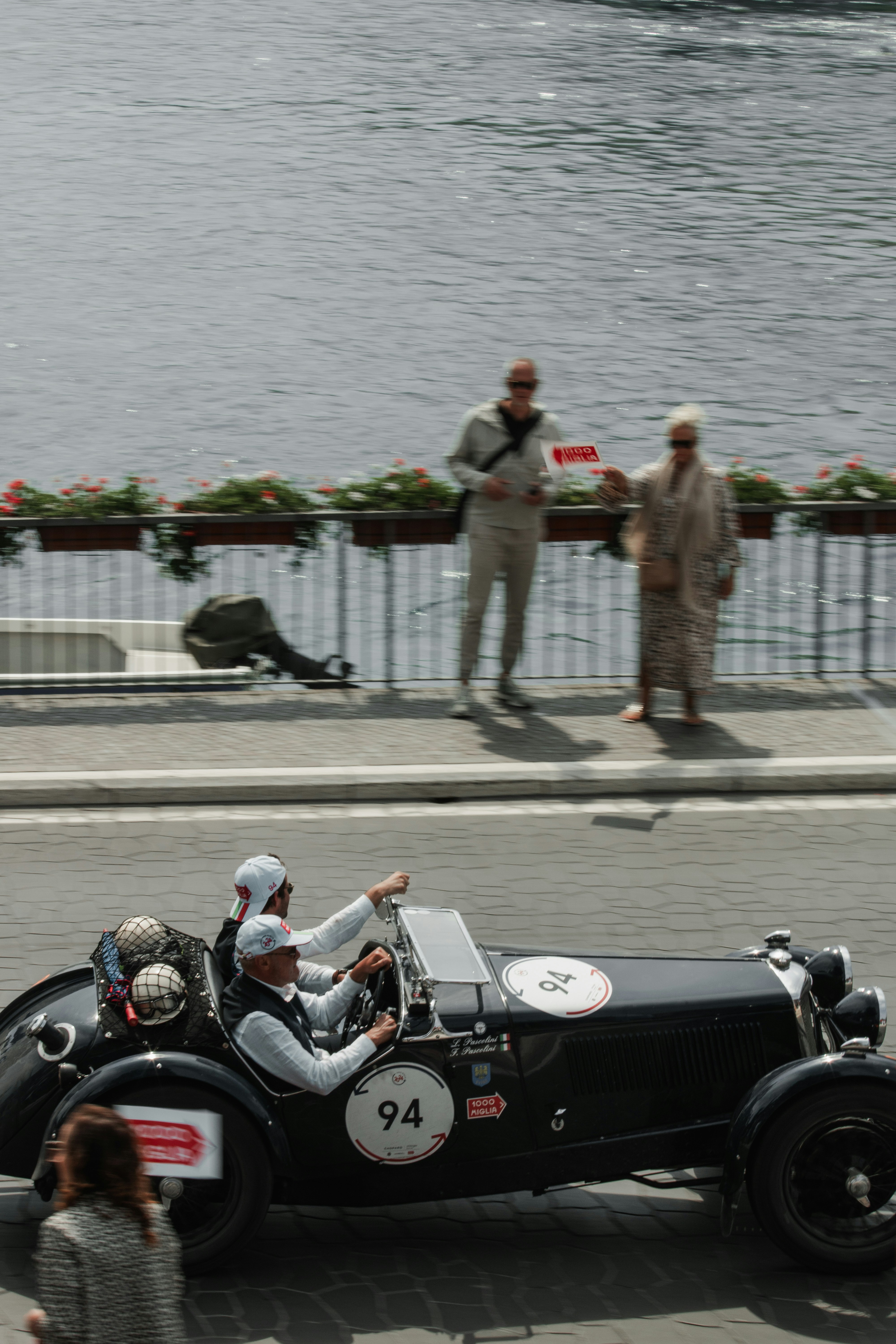 A vintage race car driving down a street next to a body of water