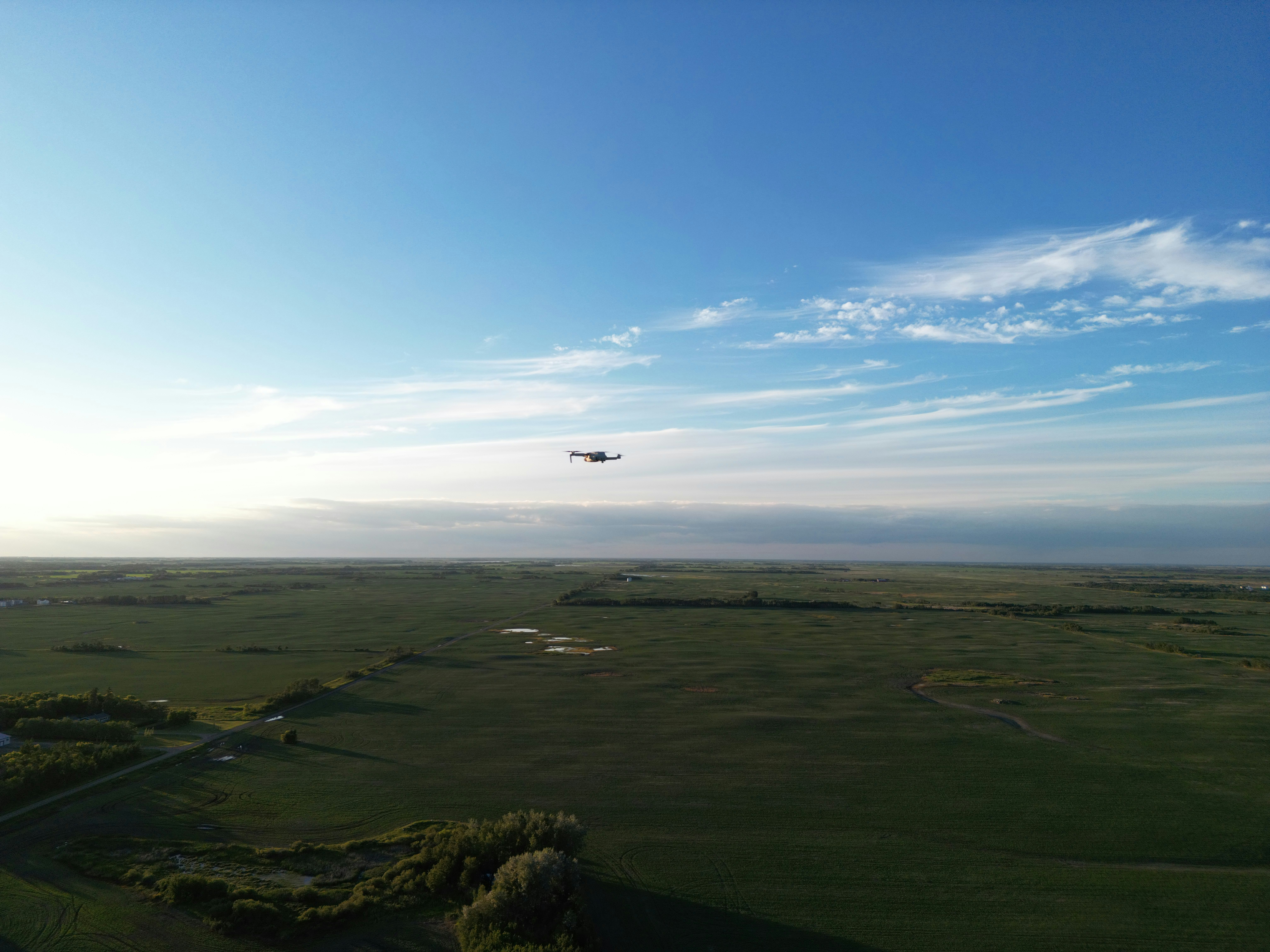 DJI drone flying over green hills with clear blue sky