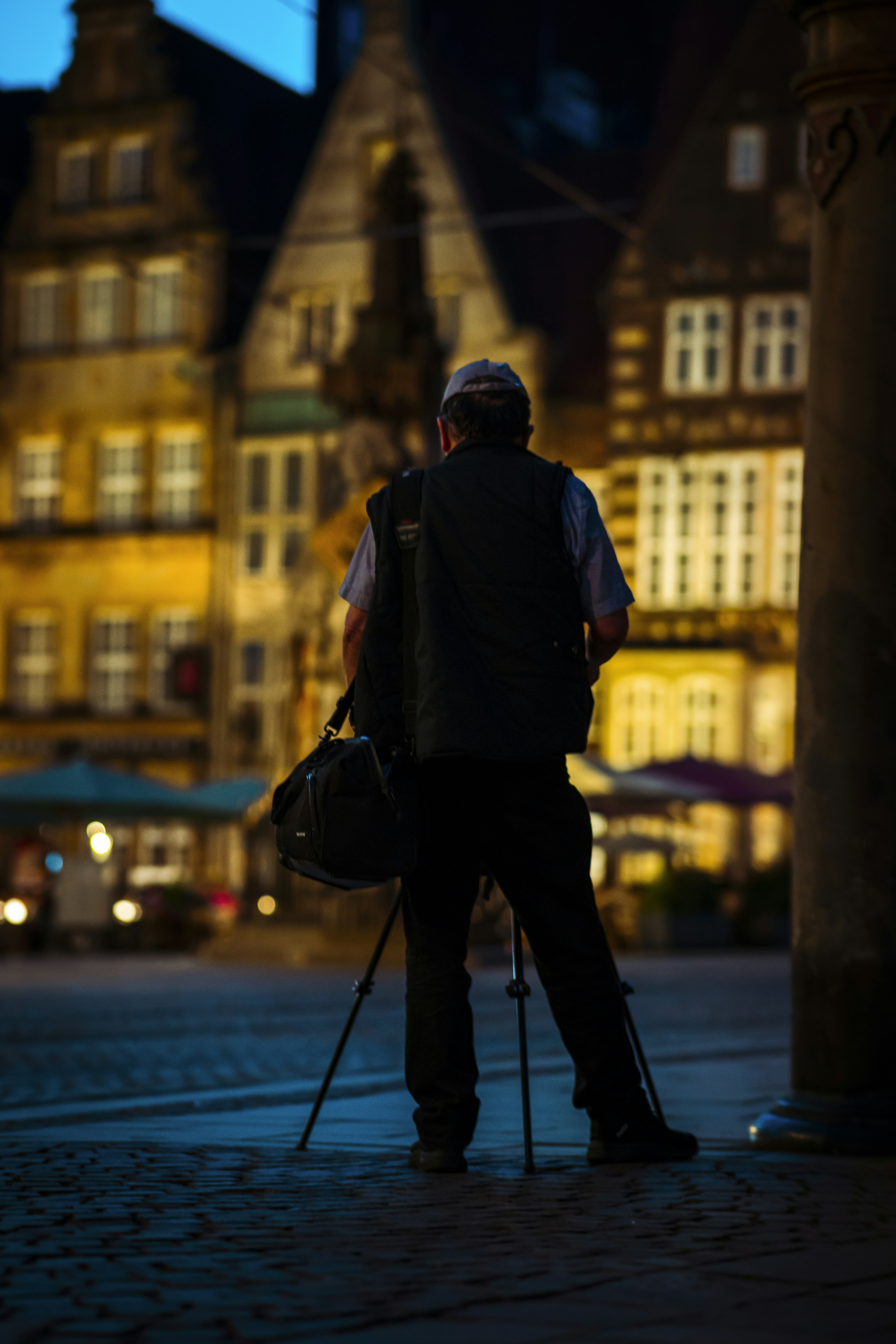 Photographer holding camera walking down a street seen from behind
