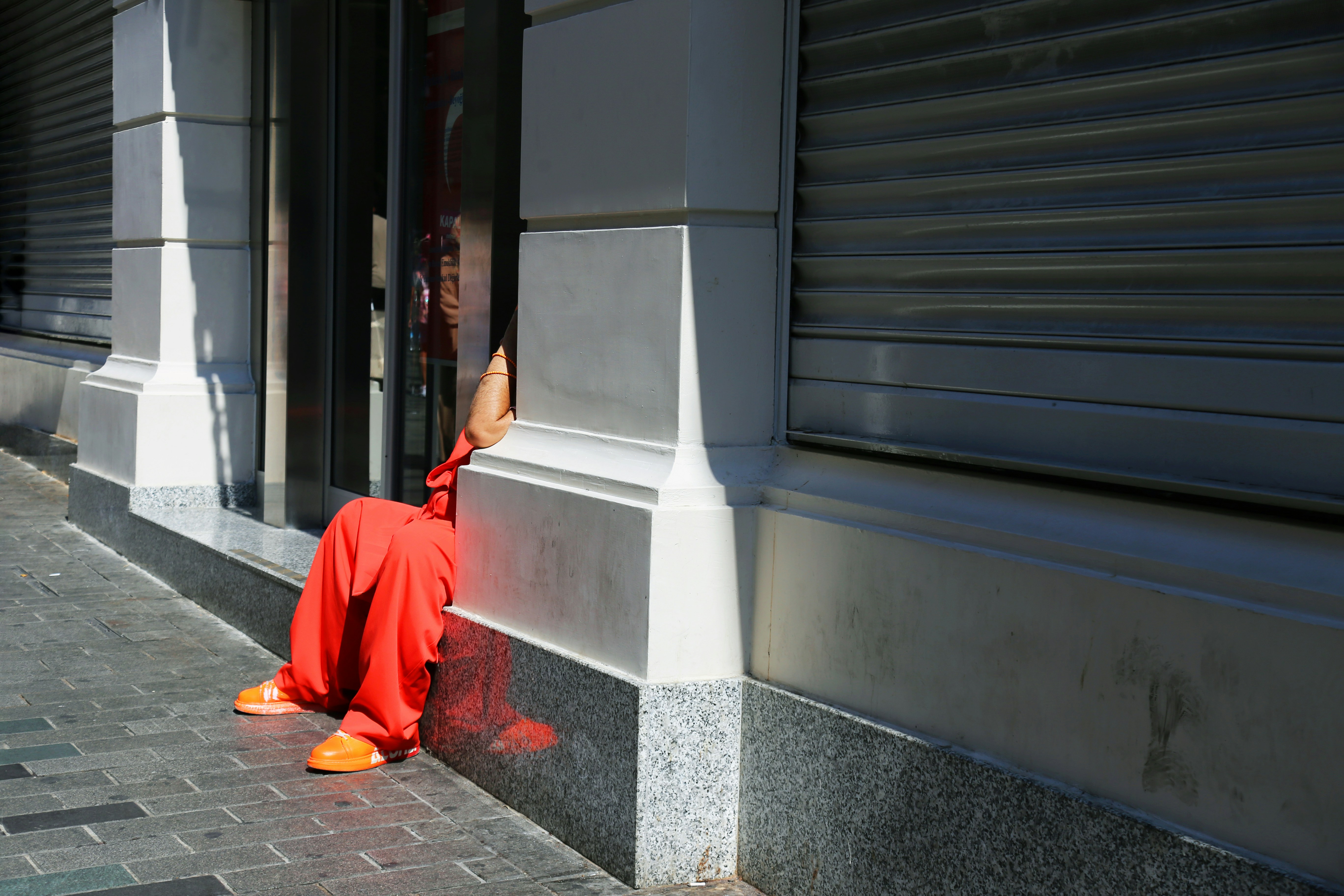 A person in orange pants leaning against a building