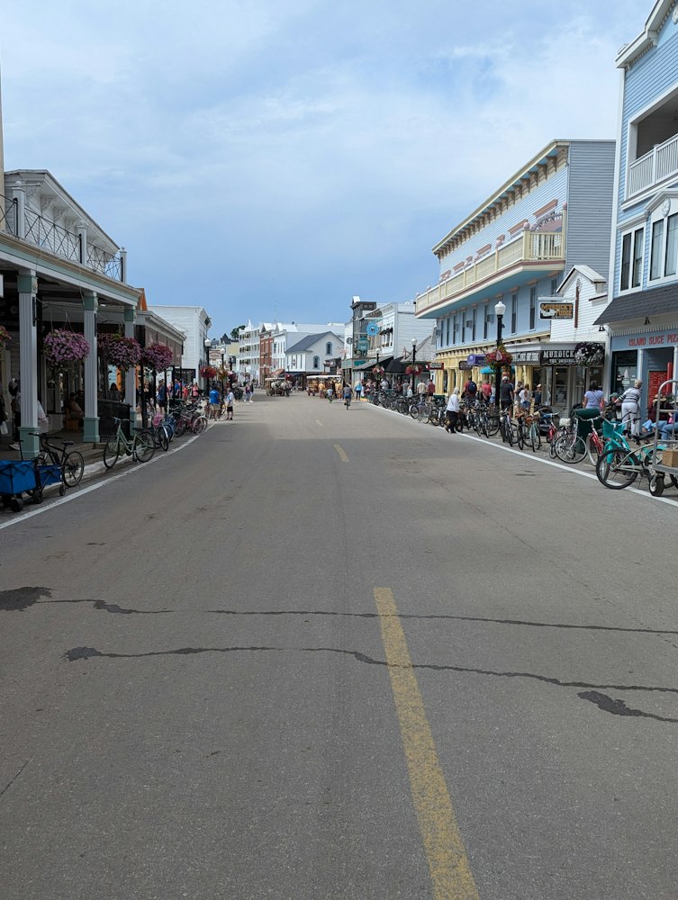 A car-free main street lined with Victorian storefronts, hanging flower baskets, and rows of parked bicycles