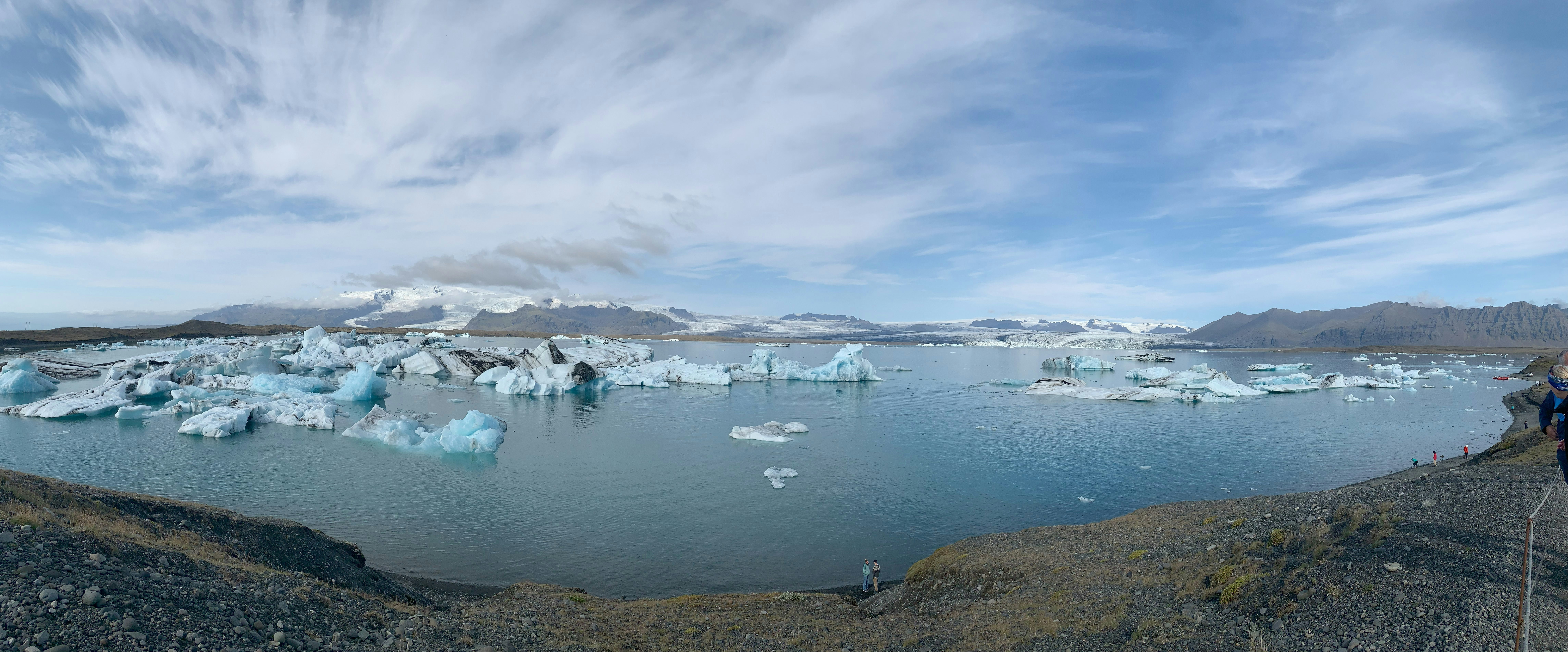 A man standing on top of a hill next to a lake filled with iceberg