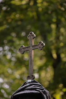 A cross on top of a statue with trees in the background