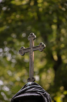 A cross on top of a statue with trees in the background