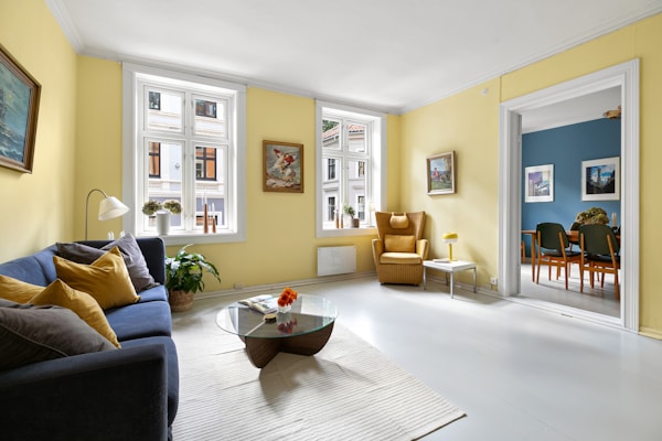 Дневна със синьо‑зелено канапе, горчичен фотьойл и жълти стени, създаващи уютна и приветлива атмосфе