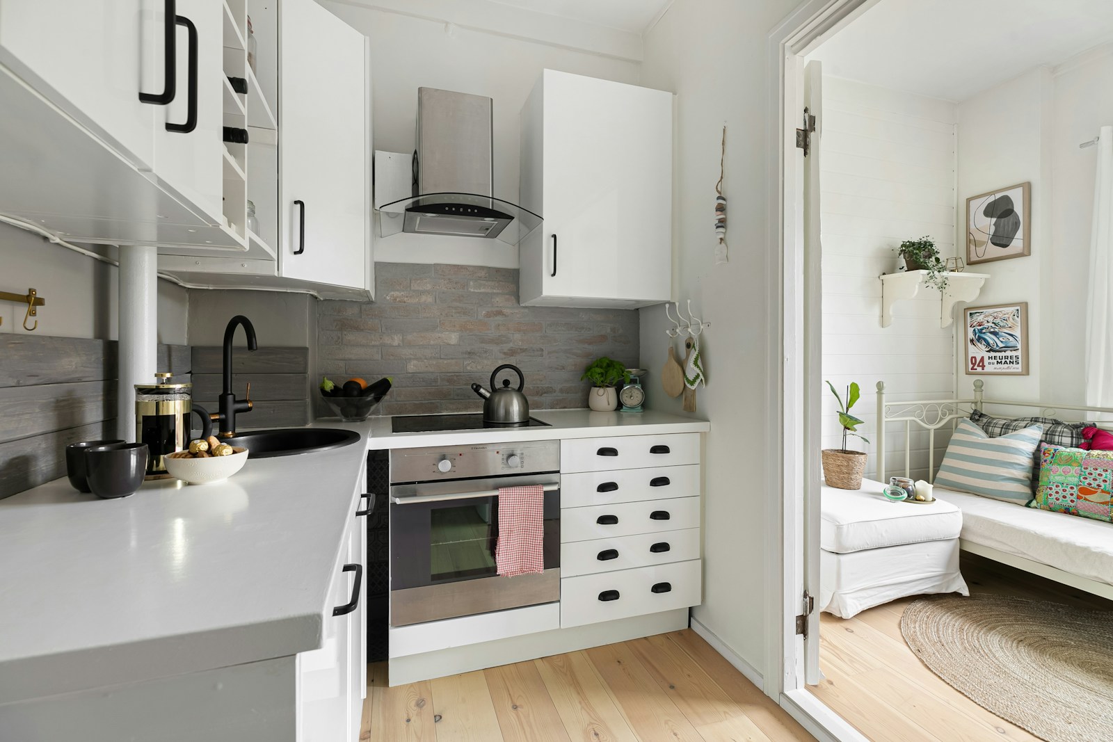 small white kitchen with hood vent, open shelves, and warm light