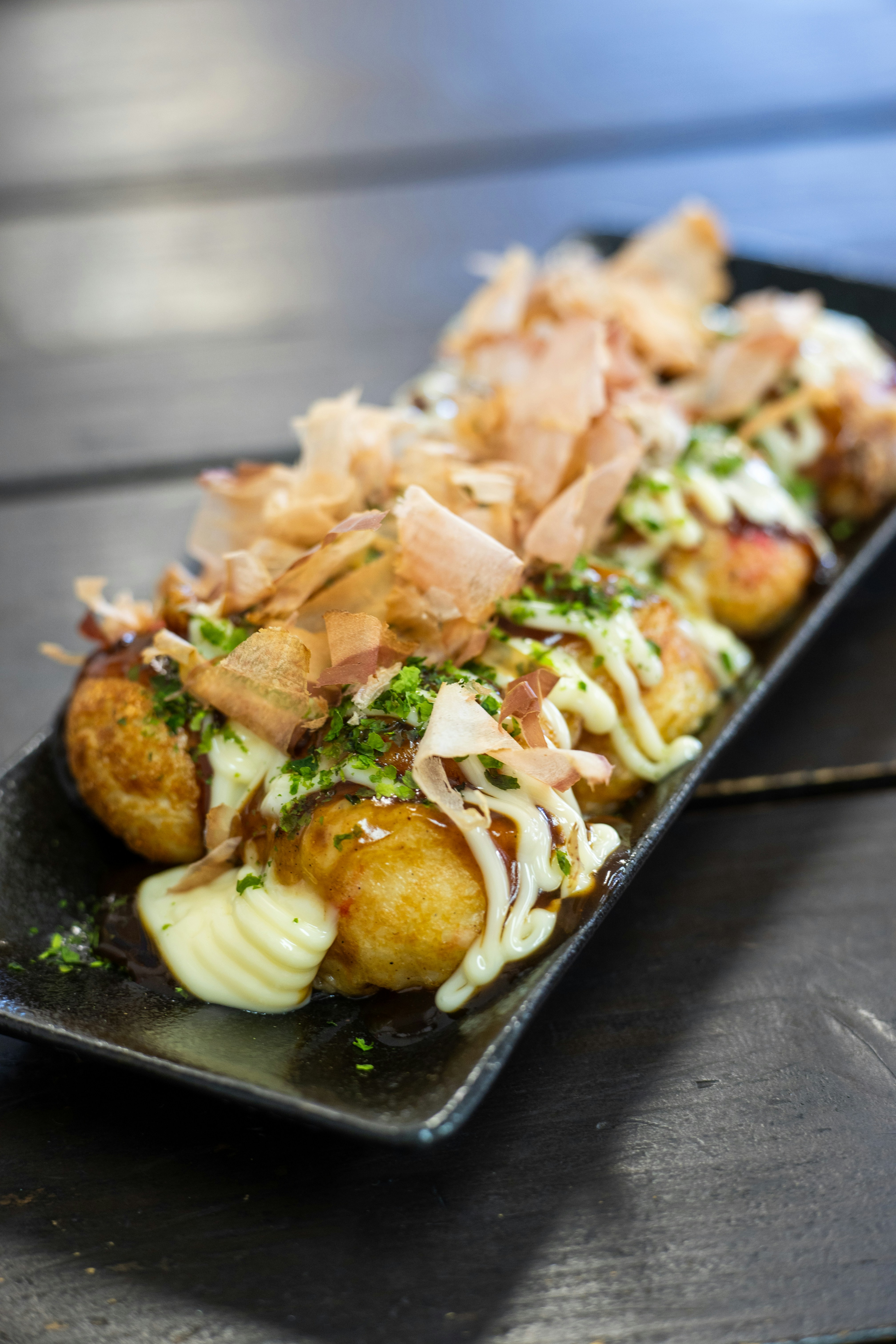 Finished takoyaki balls topped with sauce, mayo, bonito flakes, and green onions`