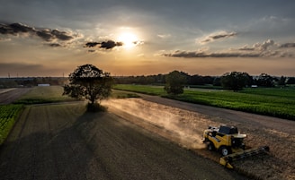 A tractor driving down a dirt road next to a field