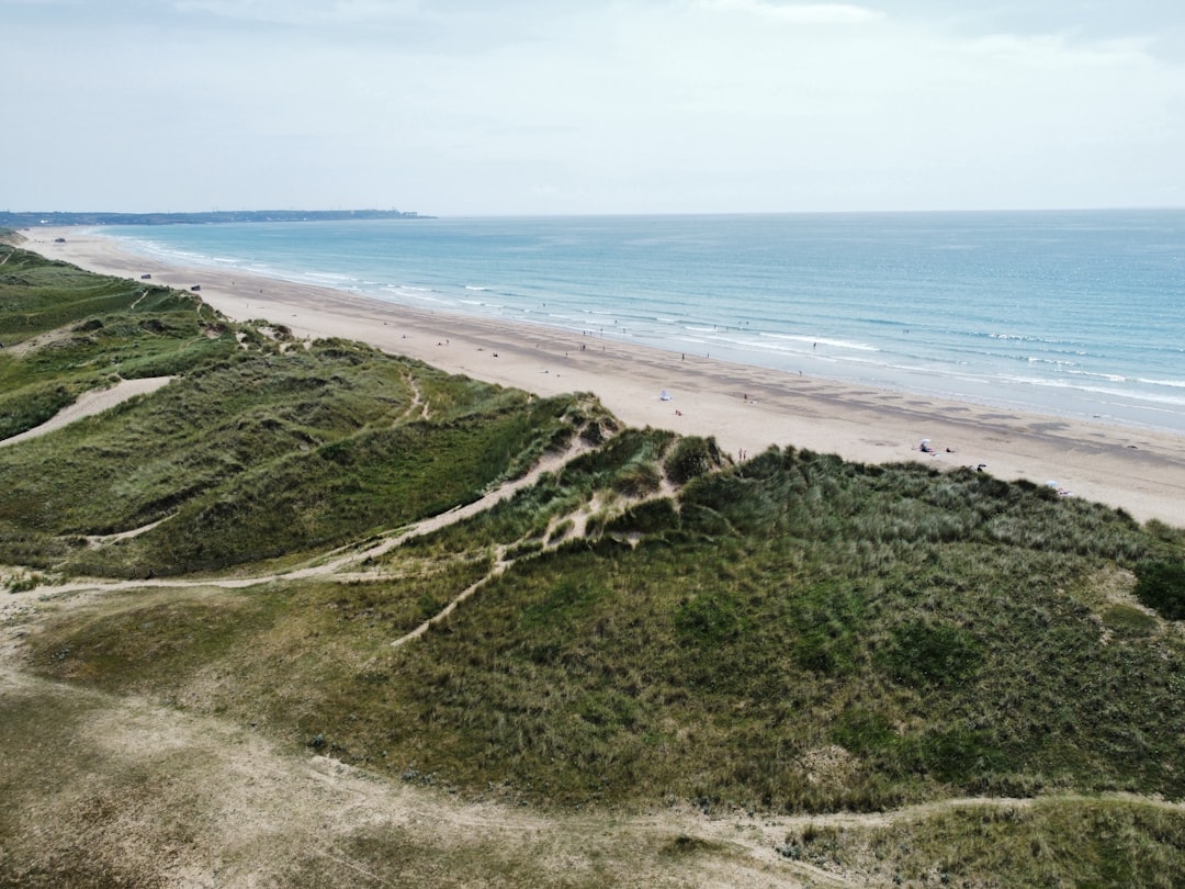 A sandy beach next to the ocean under a cloudy sky, Normandy dunes