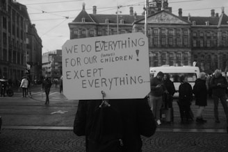A man holding a sign that says we do everything for our children except everything