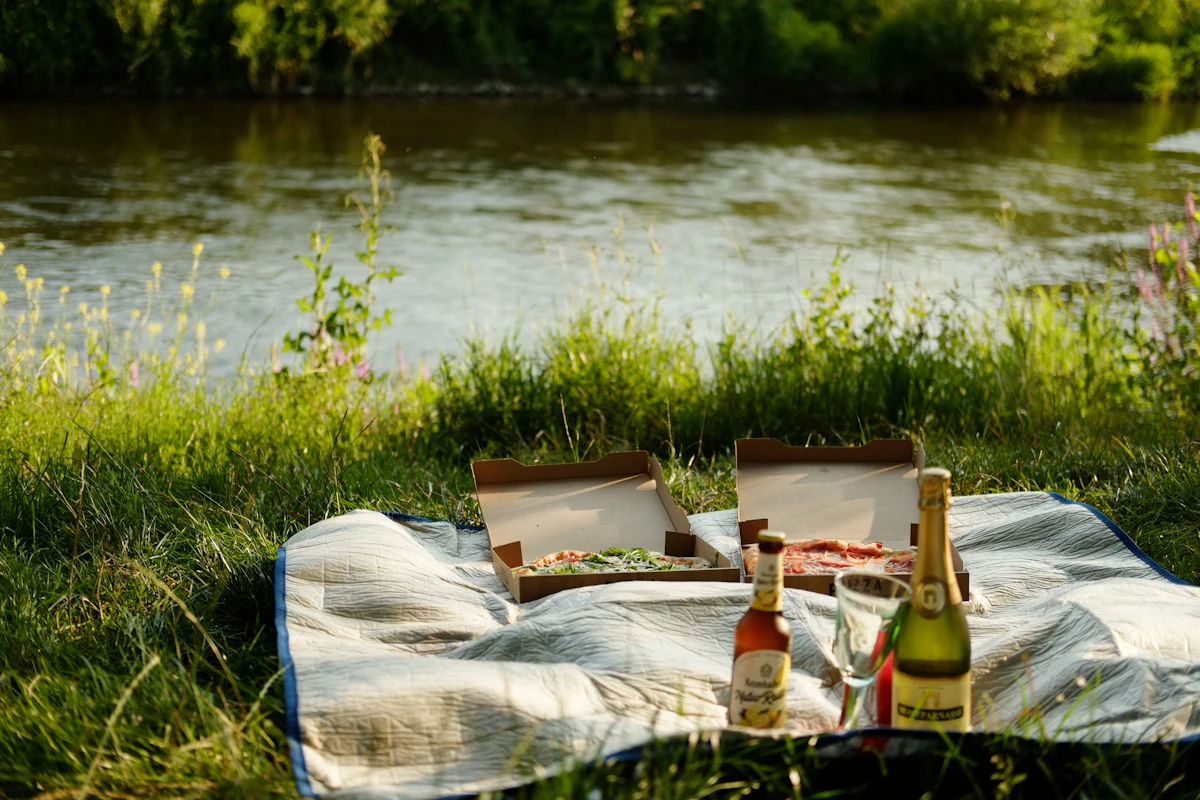 Two bottles of wine and two bottles of wine on a blanket near a river