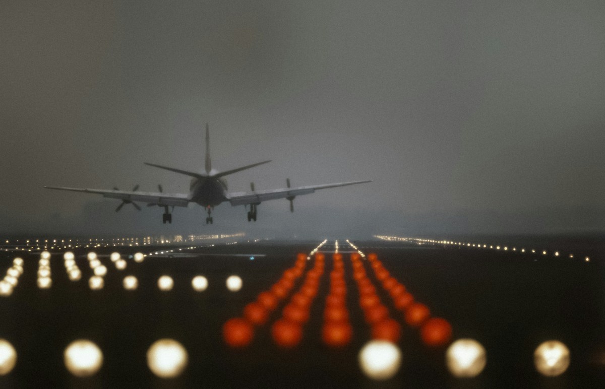 เครื่องบินกำลังร่อนลงบนรันเวย์ยามพลบค่ำพร้อมไฟนำร่อน
