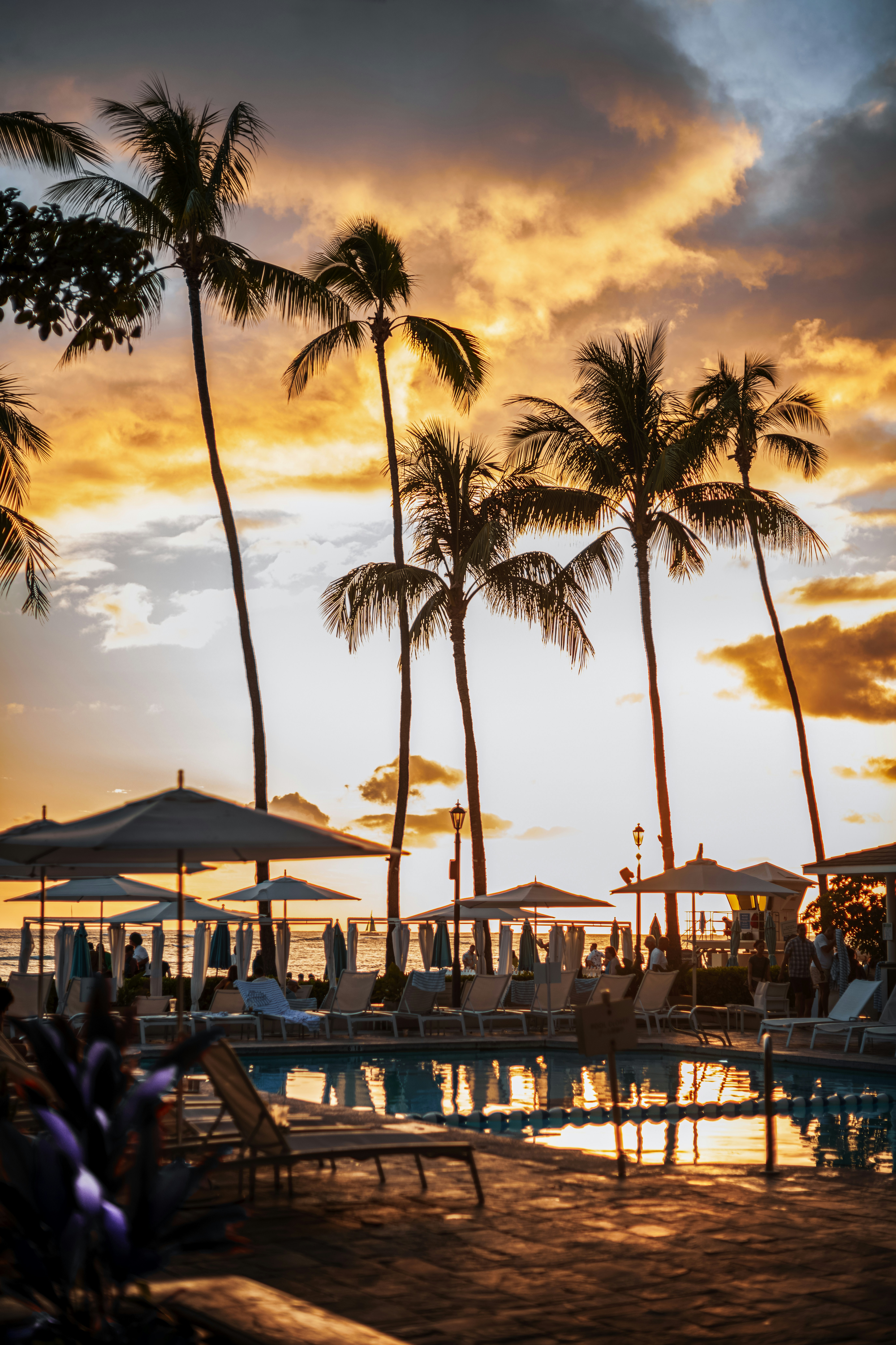 A sunset view of a resort pool with lounge chairs and umbrellas