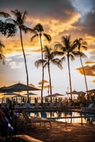 A sunset view of a resort pool with lounge chairs and umbrellas