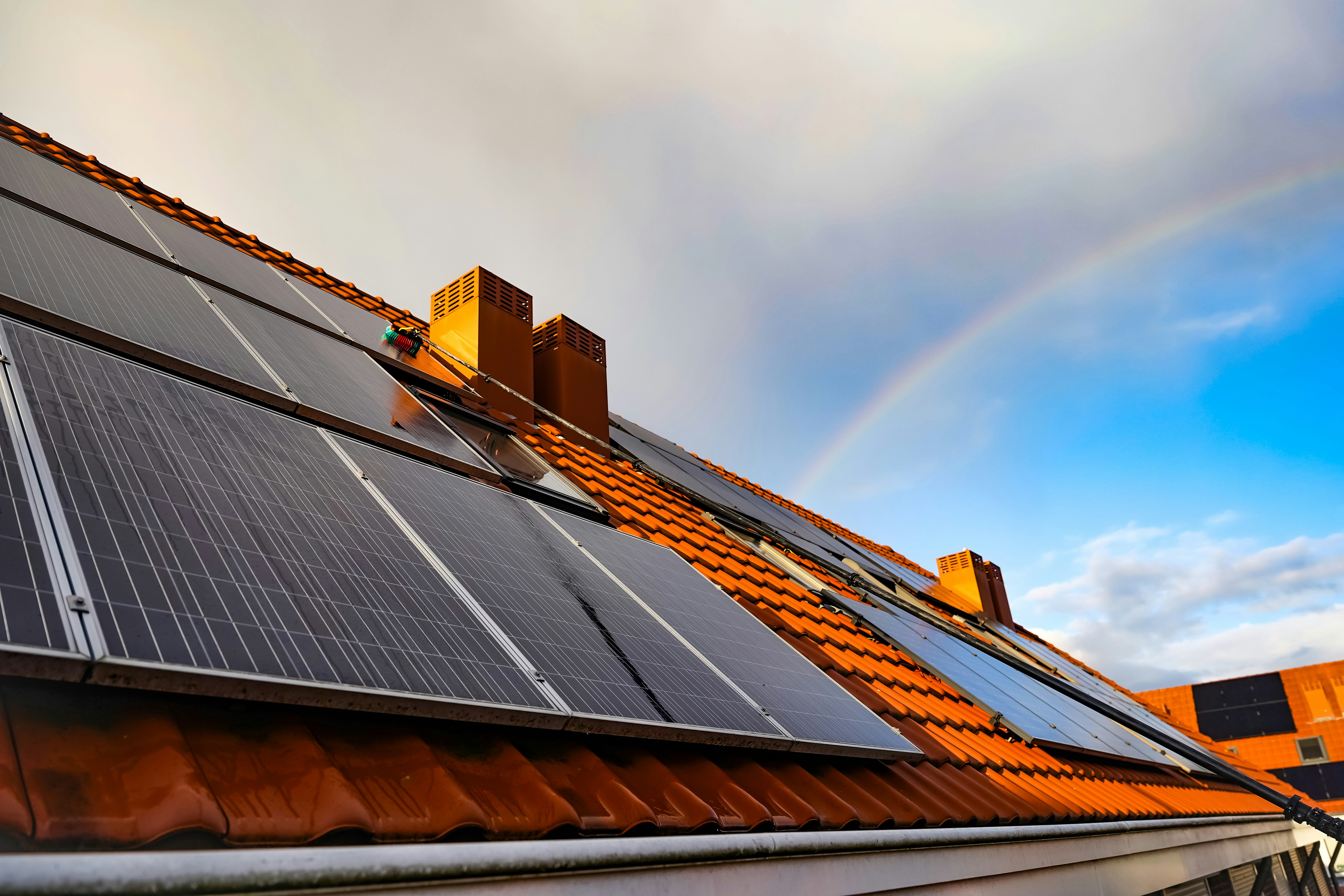 A solar panel on a roof with a rainbow in the background