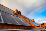 A solar panel on a roof with a rainbow in the background