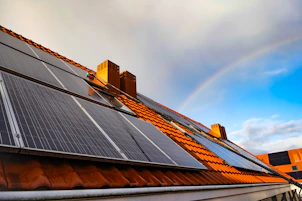 A solar panel on a roof with a rainbow in the background