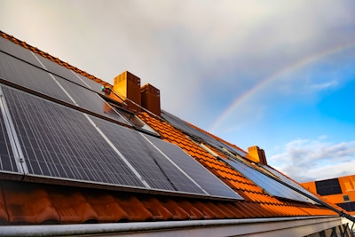 A solar panel on a roof with a rainbow in the background