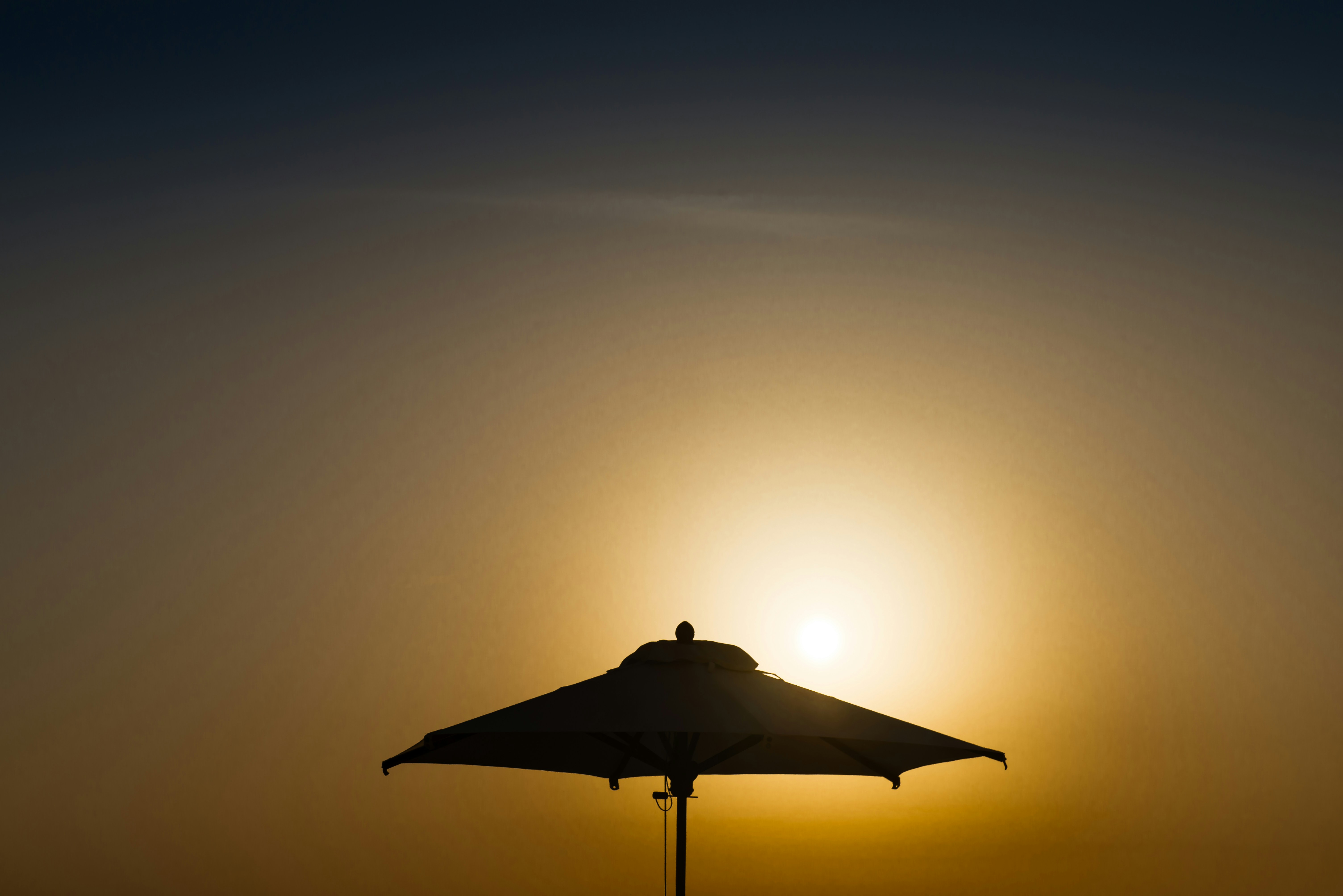 해변 파라솔 너머로 해가 지고 있습니다