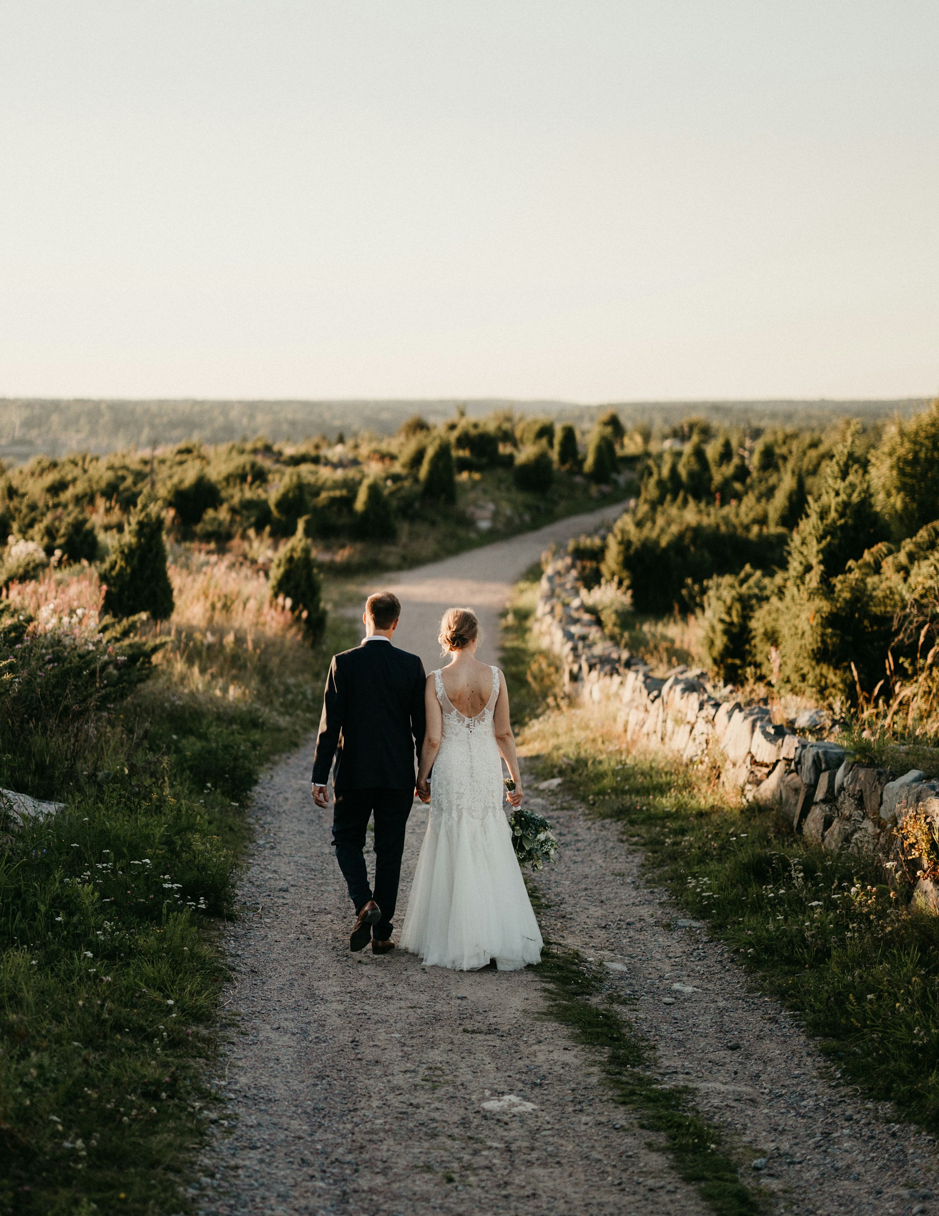 A bride and groom walking down a dirt road