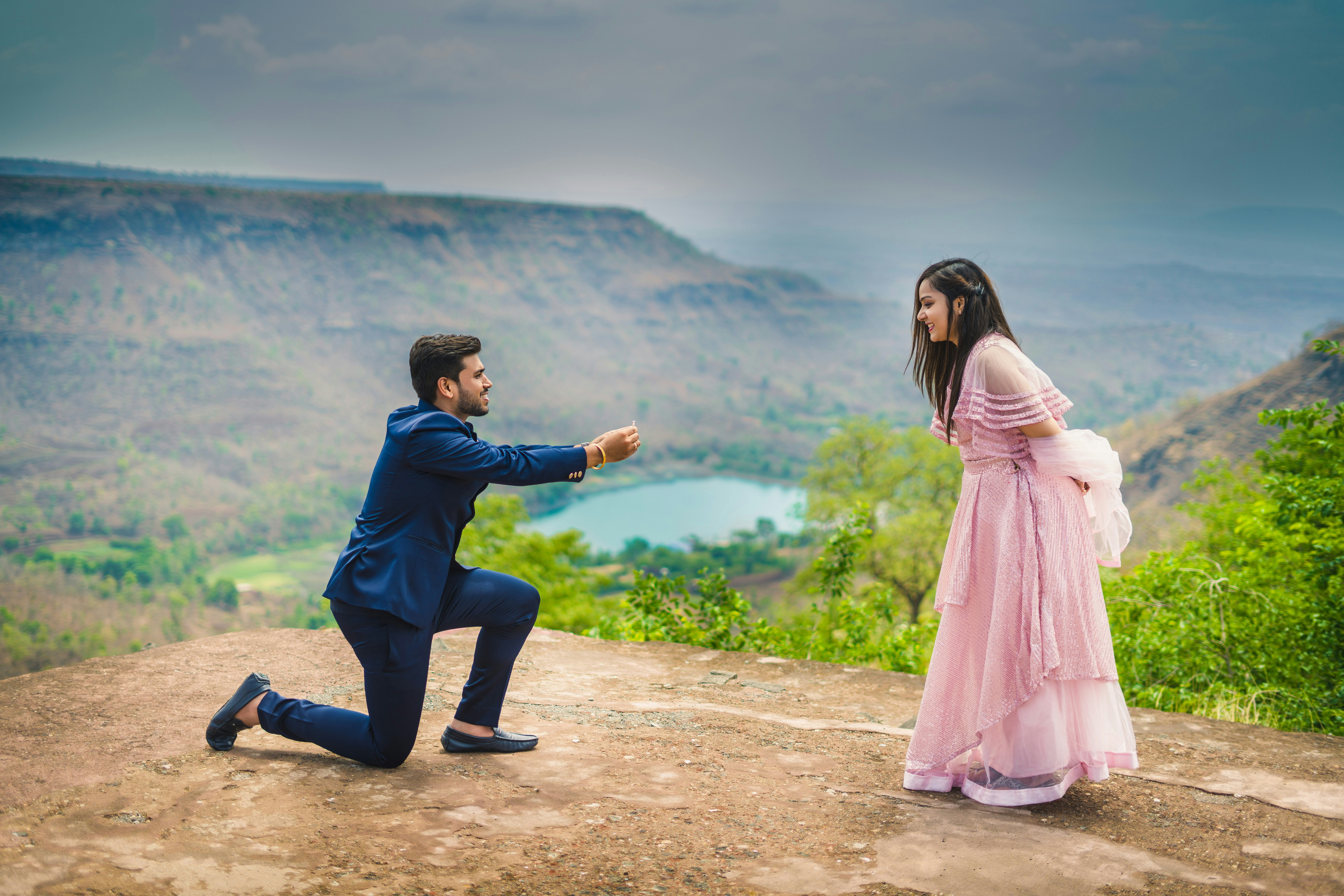 A man kneeling down next to a woman in a pink dress