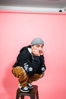 A man sitting on a stool in front of a pink wall