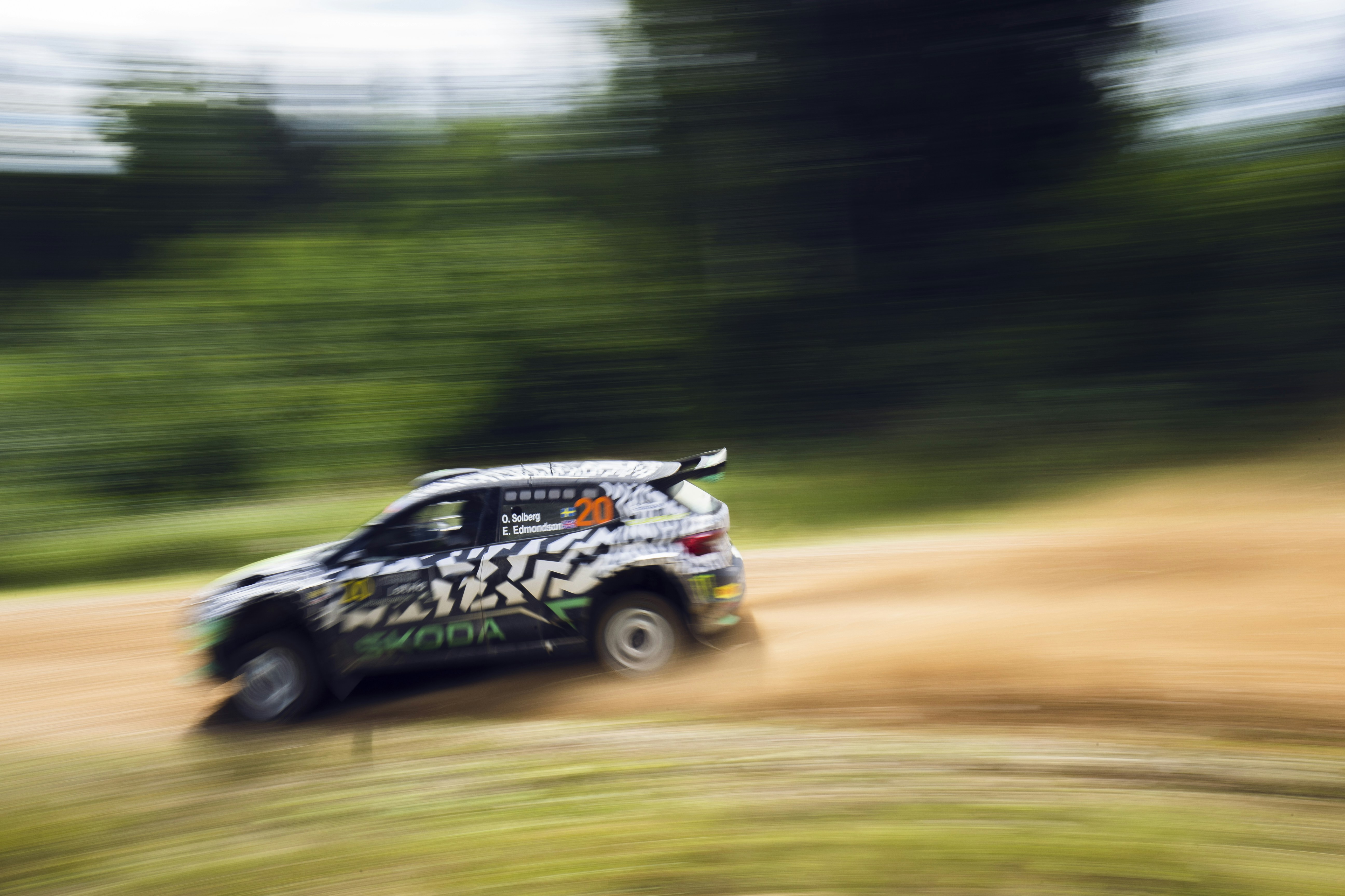 A car driving down a dirt road with trees in the background