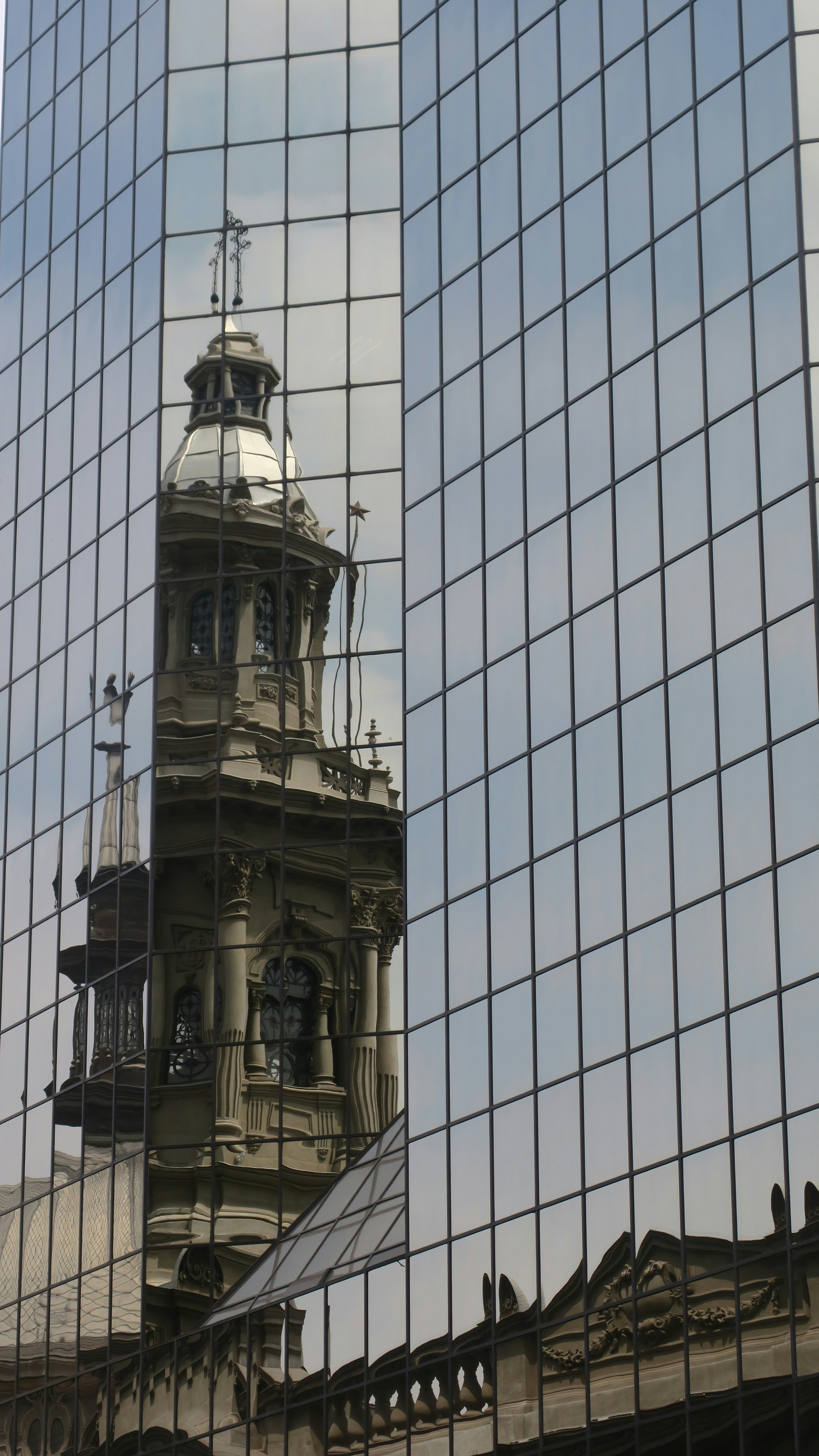 A clock tower is reflected in the windows of a building
