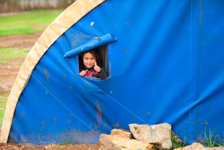 A little girl peeking out of a blue tent