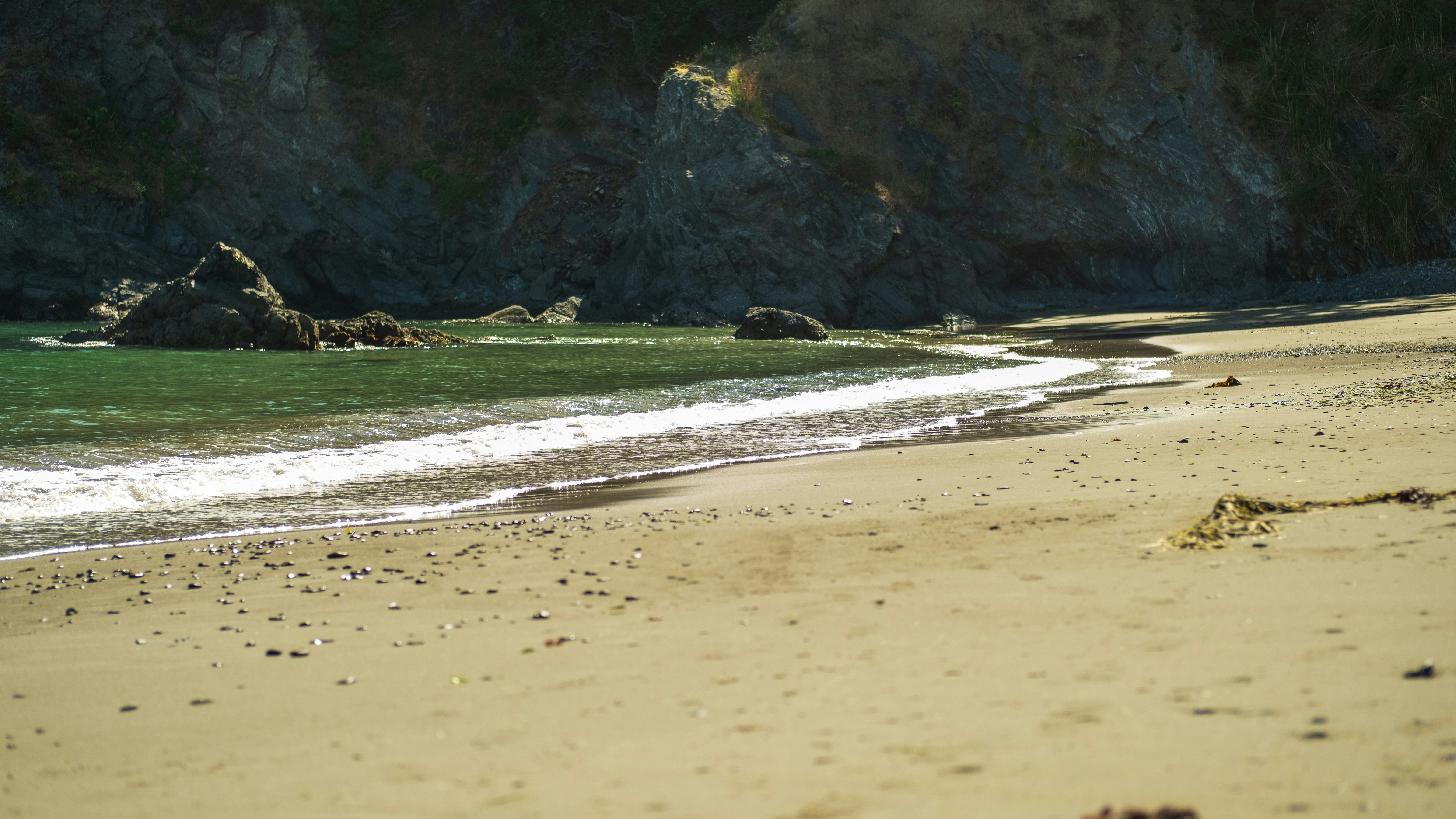 A sandy beach next to the ocean with a cliff in the background, 