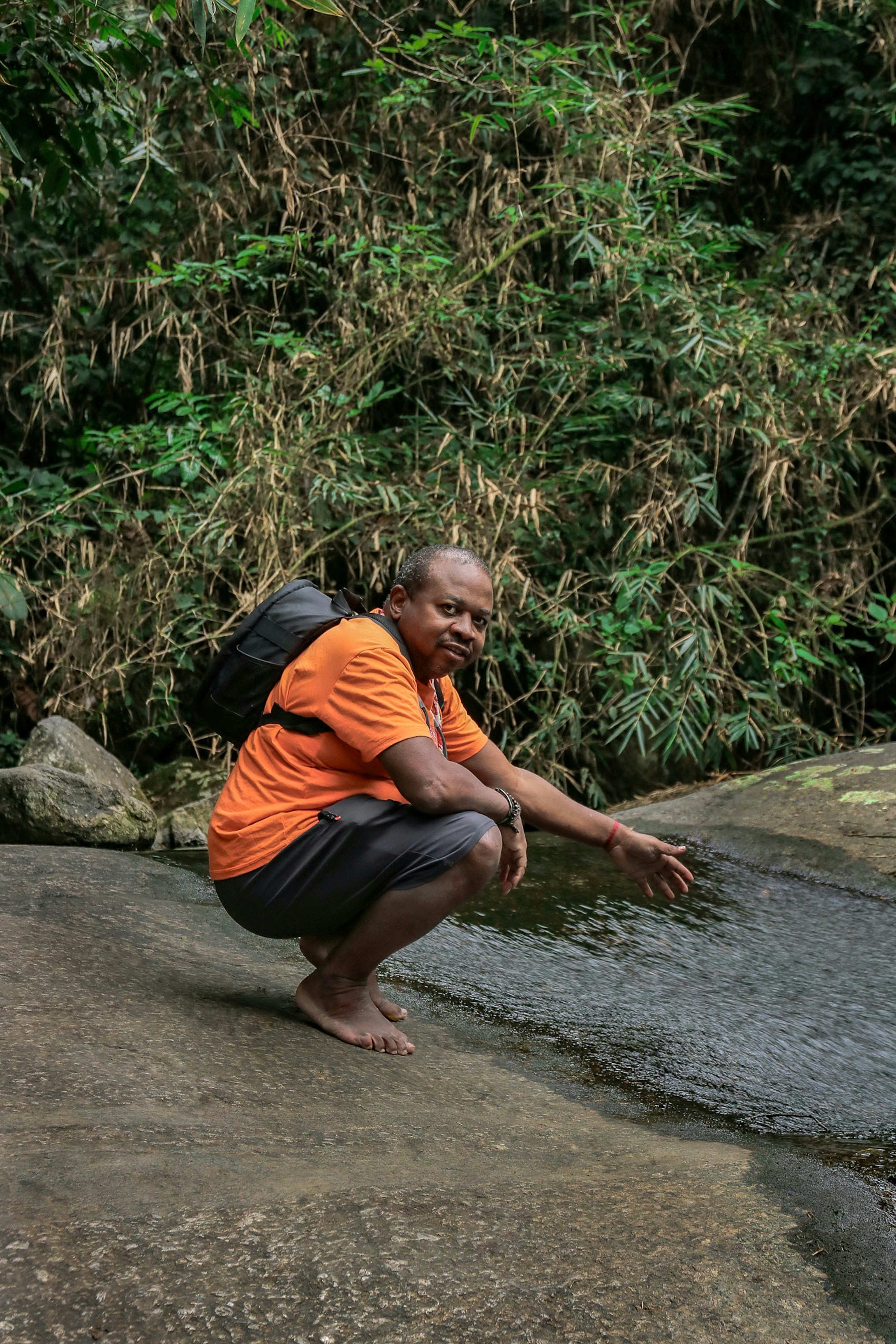 A man squatting on a rock next to a river