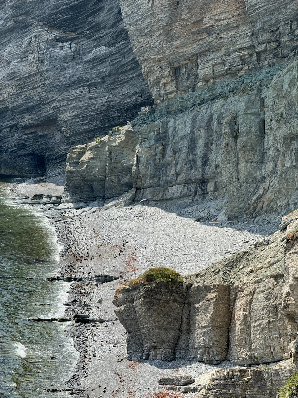 Rocky cliff face with sandy beach and crashing waves in a rugged coastal landscape