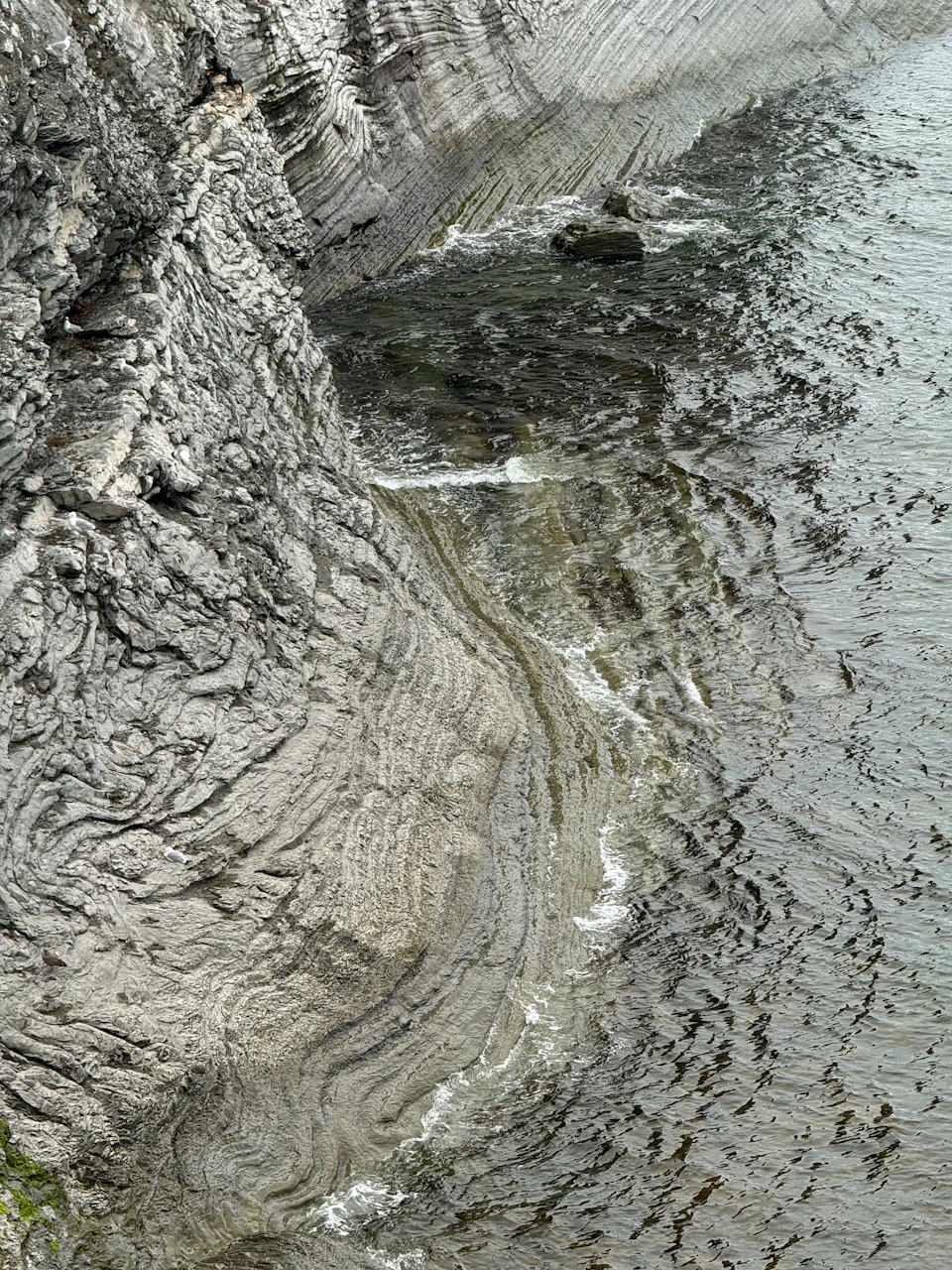 Rock formations on cliff face display contrasting textures of gray, jagged and smooth rocks