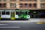 A green and white trolley traveling down a street