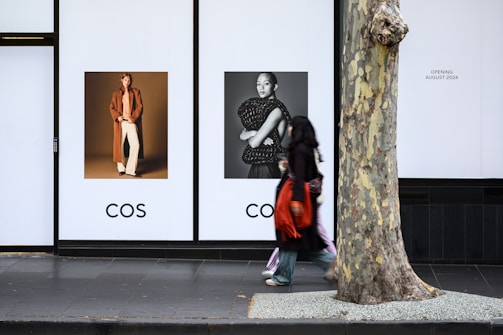 A woman walking past a tree on a sidewalk