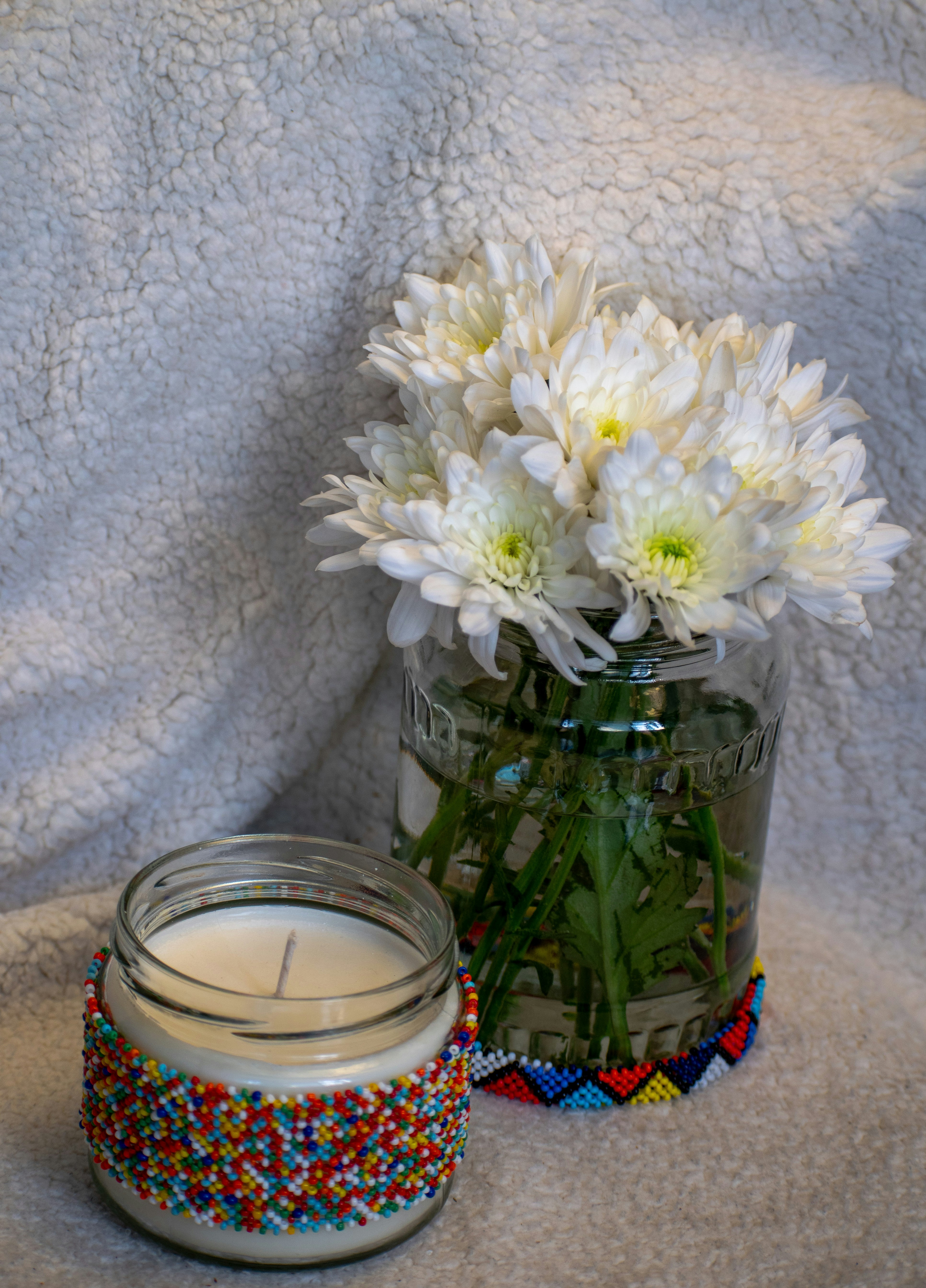 Un barattolo di vetro pieno di fiori bianchi accanto a una candela