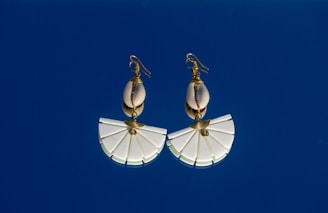 A pair of white umbrella shaped earrings against a blue sky
