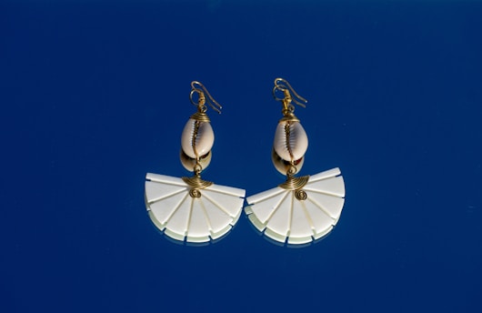 A pair of white umbrella shaped earrings against a blue sky