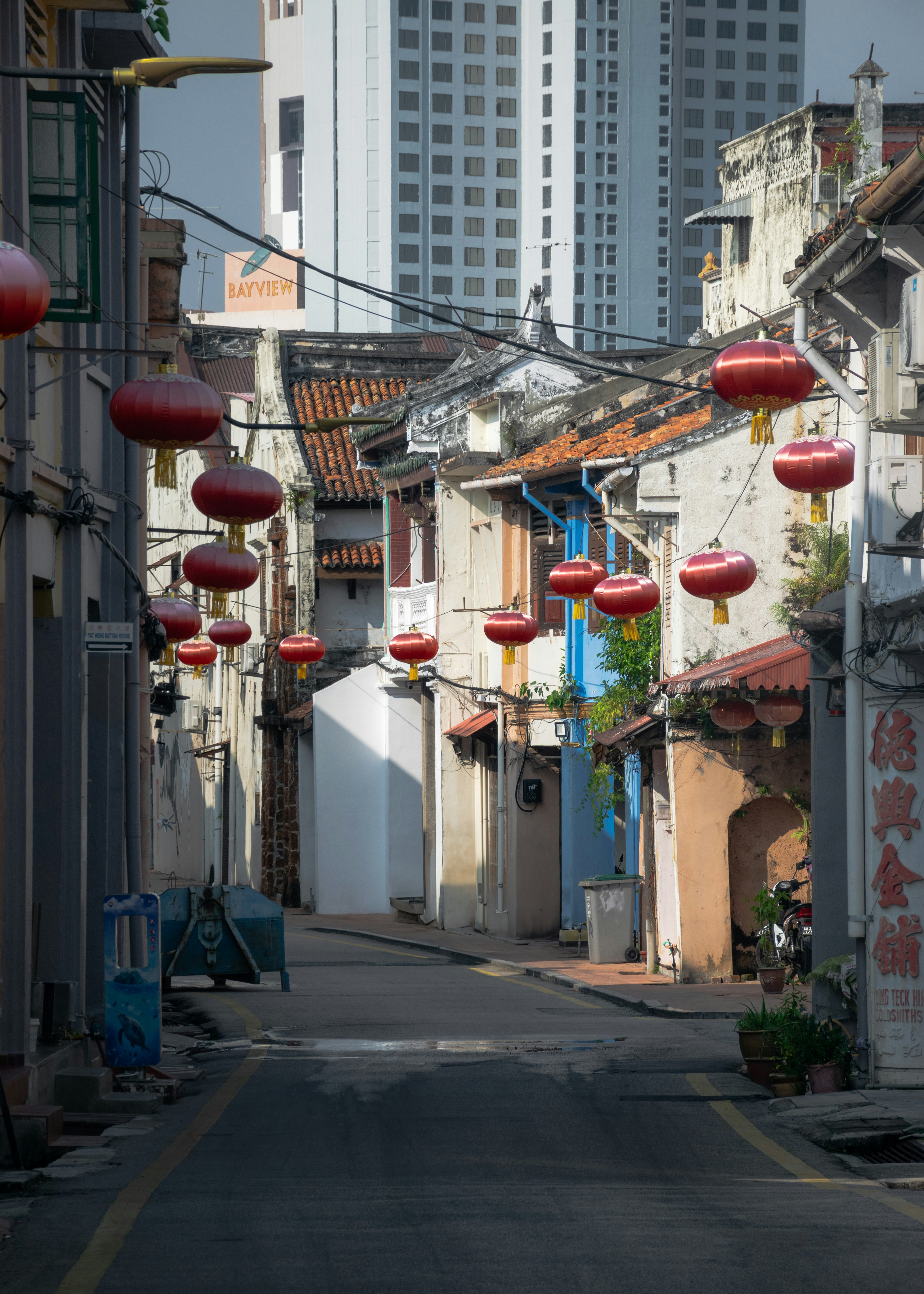A narrow street with chinese lanterns hanging from the buildings