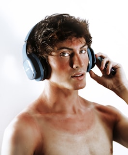 A shirtless man with headphones on talking on a cell phone