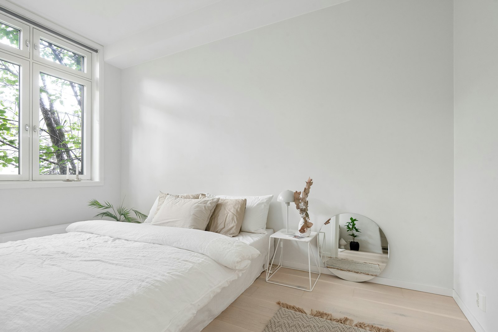 A bright white bedroom with a low bed beneath a large window