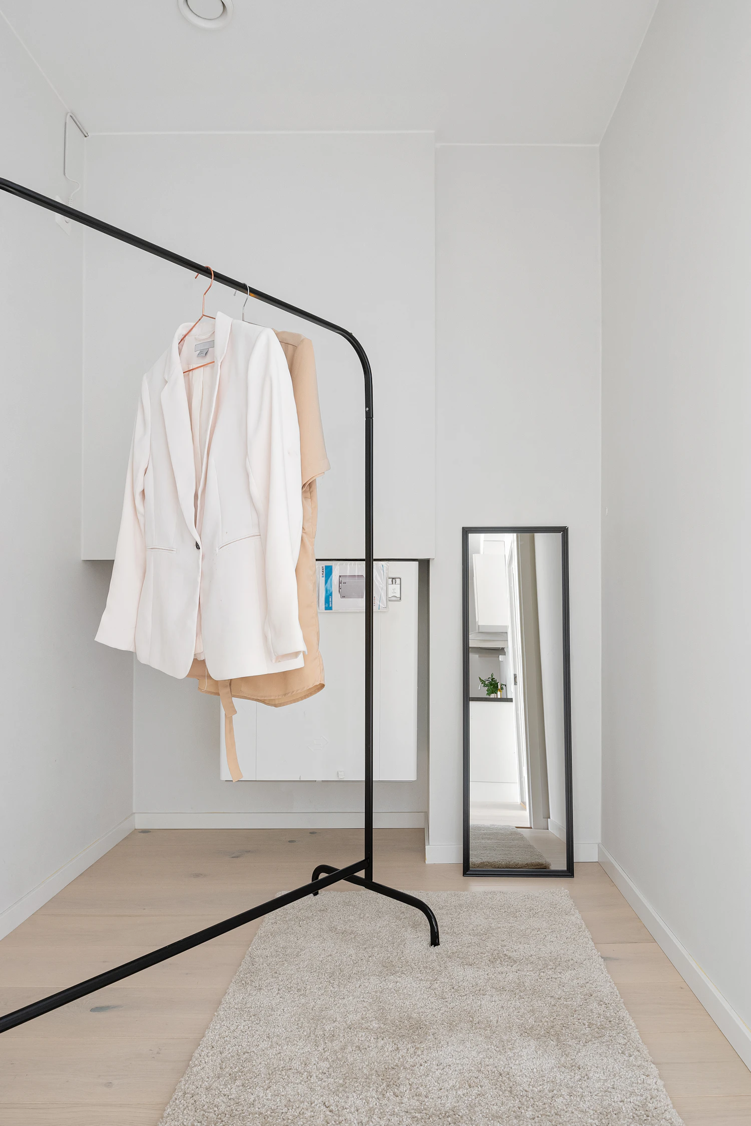 A white room with a steel coat rack and a tall leaning mirror