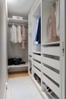 A walk in closet with white shelving and drawers