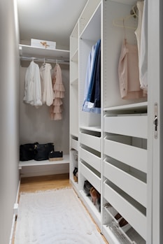 A walk in closet with white shelving and drawers