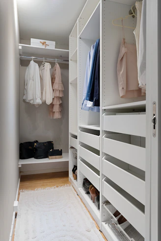A walk in closet with white shelving and drawers