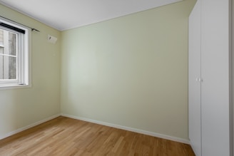 An empty room with a window and hard wood floor