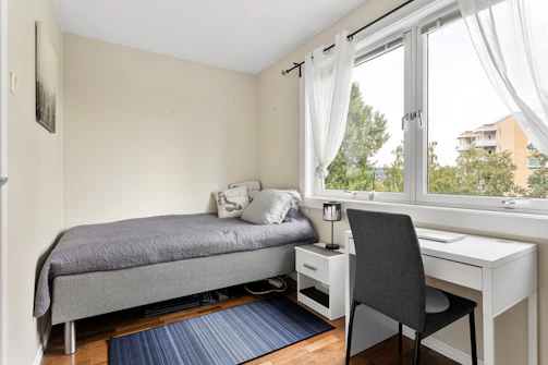 A bedroom with a bed, desk, and window