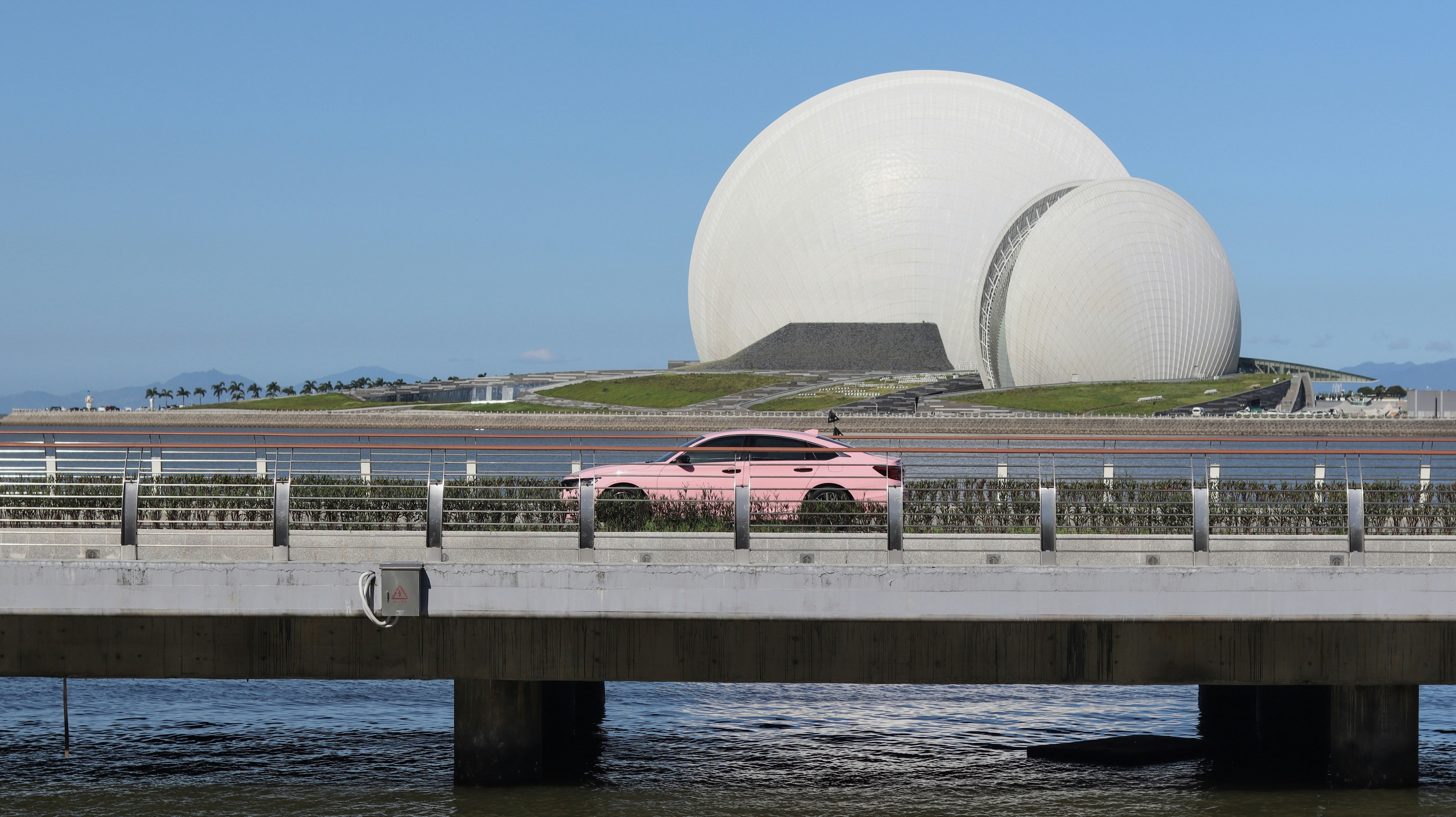 A pink car is driving across a bridge
