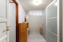 A narrow hallway with white walls and a wooden door